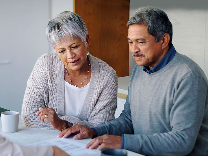 Exchange Bank Trust and Investment team member seated at table with diverse older couple reviewing estate settlement paperwork.