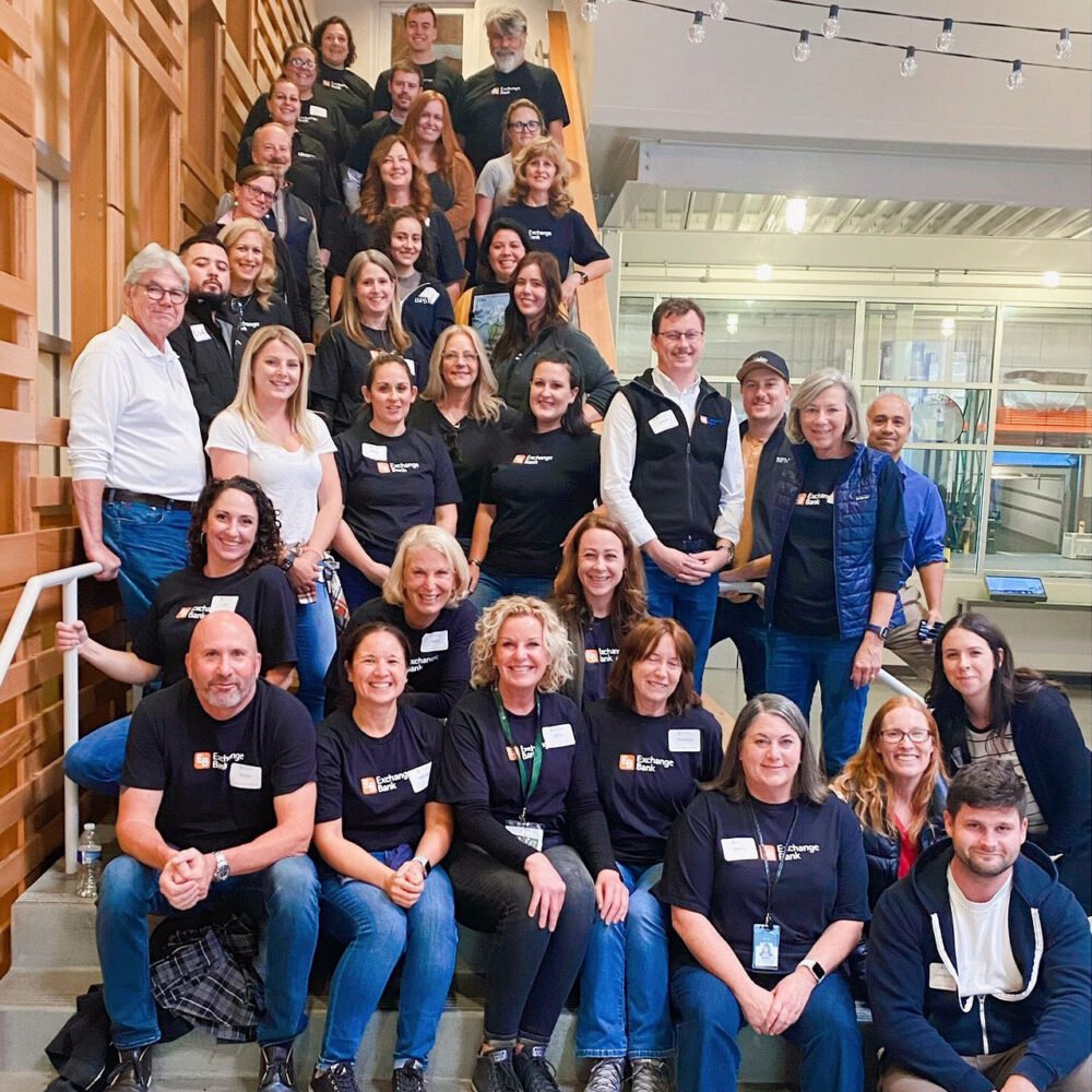 Exchange Bank employees seated and standing on staircase at Redwood Empire Food Bank of Sonoma County during a volunteer shift.