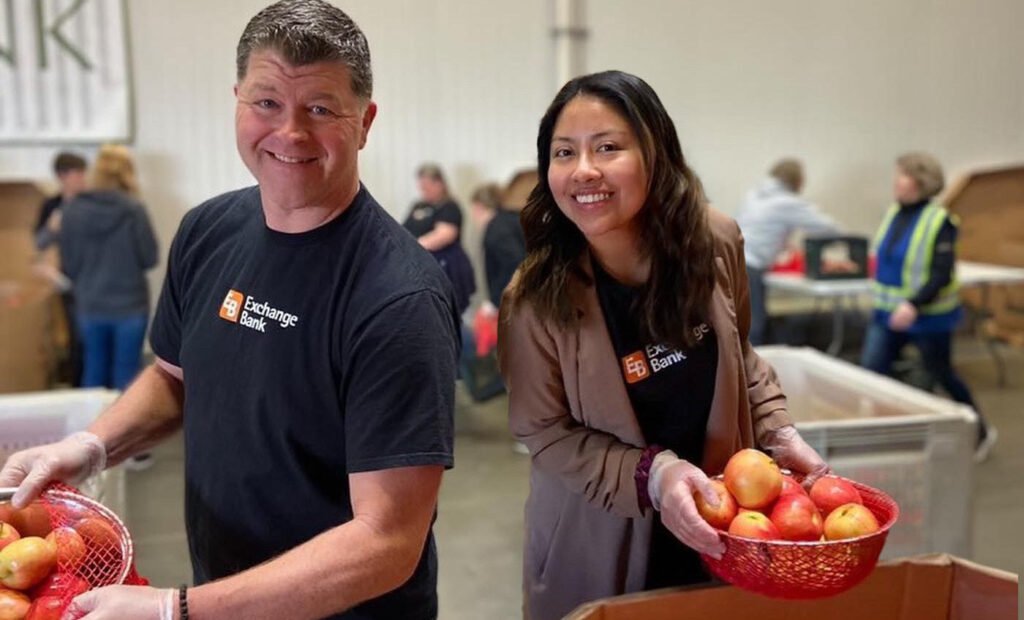 Two Exchange Bank employee volunteers sorting apples in the warehouse at Redwood Empire Food Bank, Sonoma County.